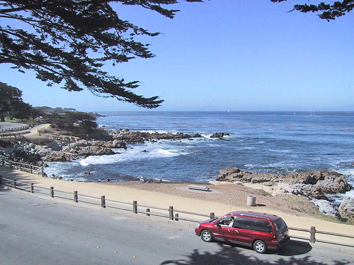 A red car is parked on the side of a road near the beach.